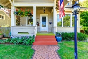 The front yard of a home with a light post in the foreground and an American flag hanging from one of the poles.