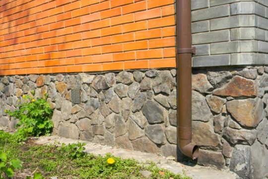 The side of a home that received foundation repair treatment from BDB Waterproofing. The exterior of the home includes rock and brick siding.