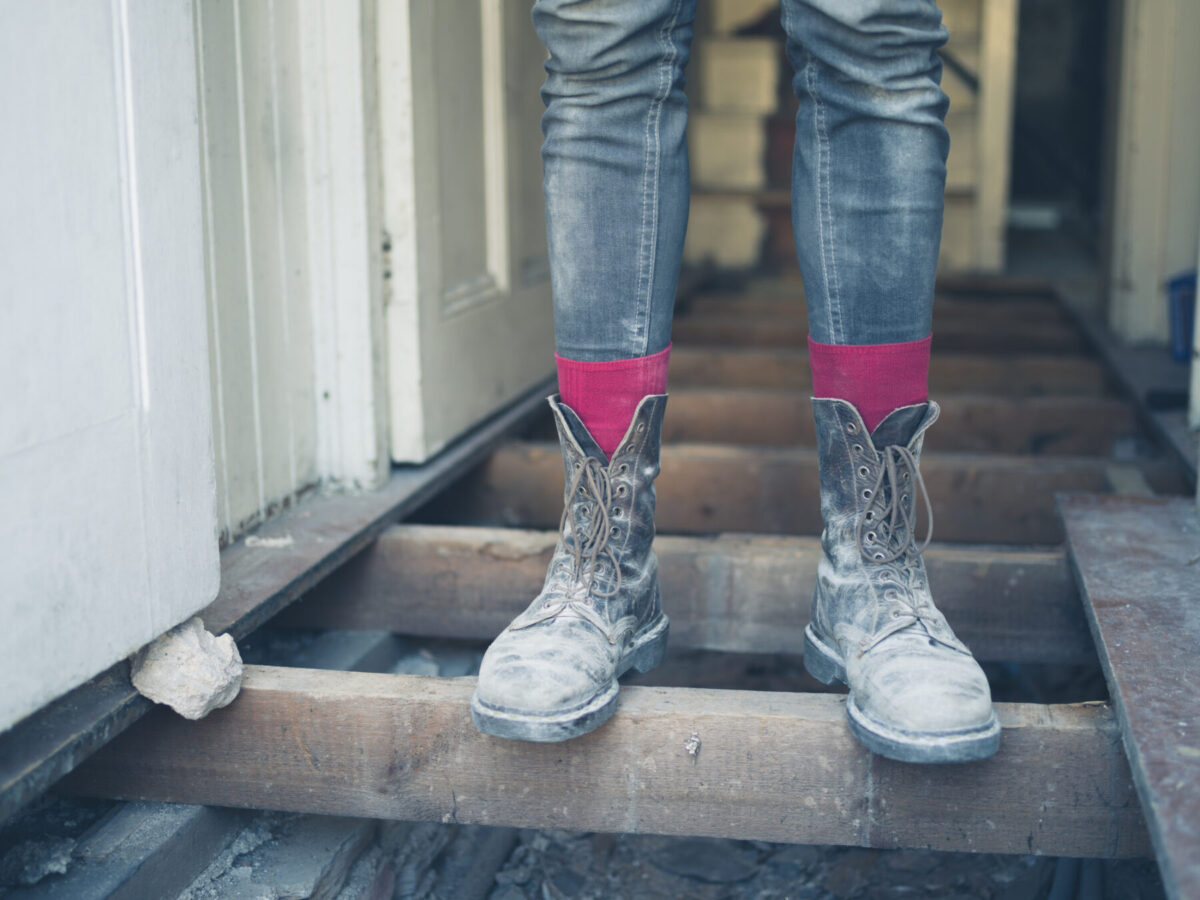 A person stands on floor joists that are holding up a floor. A sagging floor joist can cause your home problems.