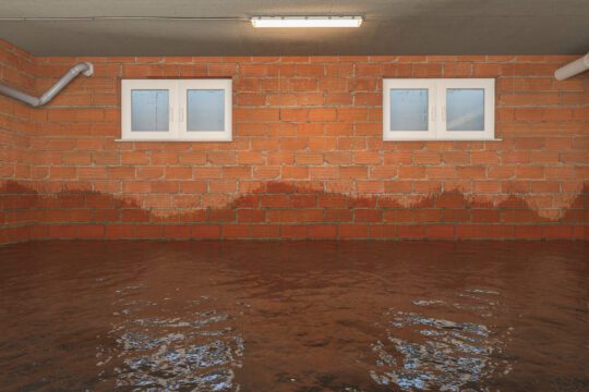A basement experiences some flooding. The brick walls are wet and the floor is completely covered with water.