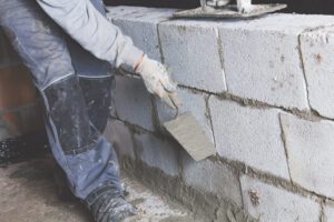 A foundation repair contractor works on a cement block foundation. The contractor is sealing in the blocks with concrete.
