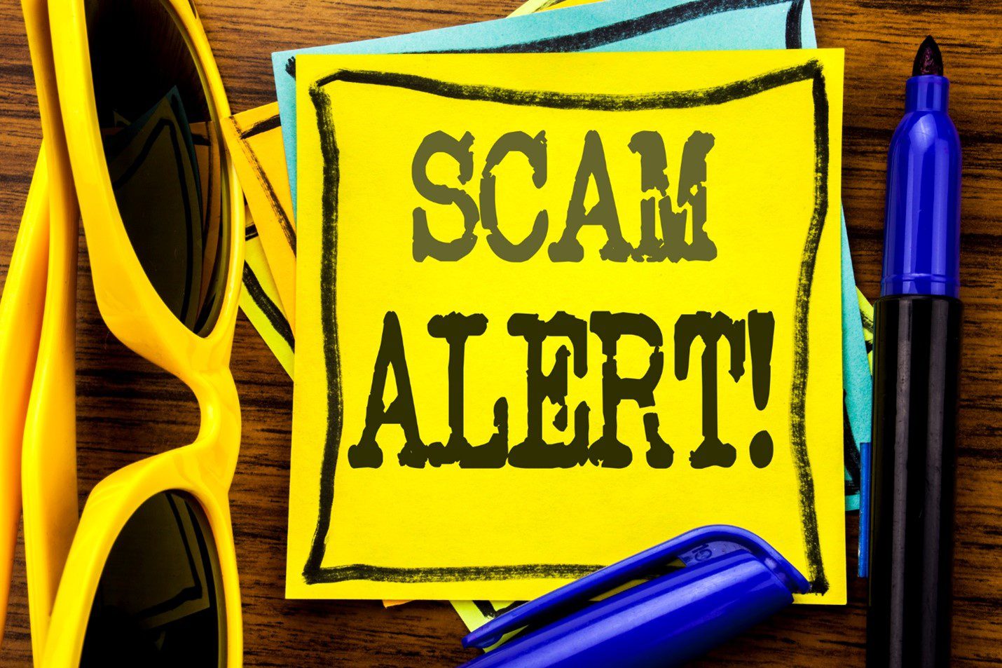 A yellow post-it note with black ink. SCAM ALERT! is written on the note.